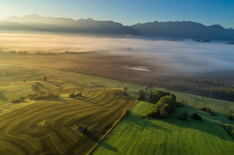 Aerial view of a meadow fertilised with liquid manure in front of a mountain landscape, morning