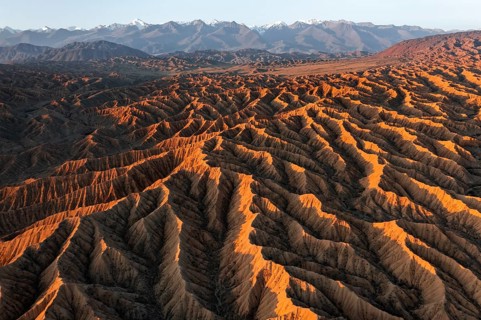 Landscape of eroded hills, badlands at sunset, mountain peaks of the Tian Shan Mountains in the