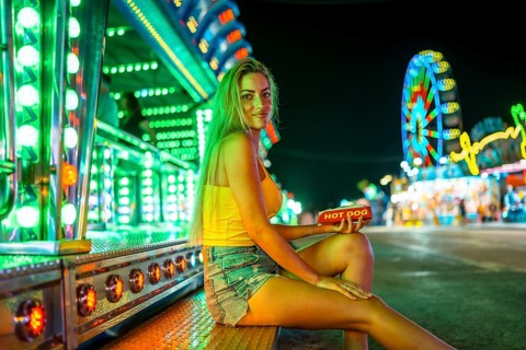 Blonde woman sitting alone about to eat a hot dog in a fair at night
