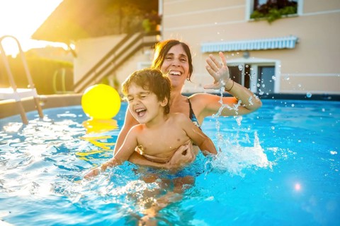 Happy mother and son are having fun, splashing and playing in a swimming pool during summer