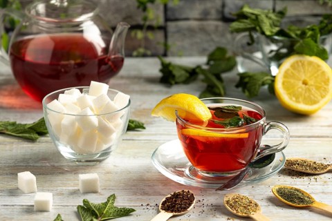 Teapot and glass with tea, lemon and mint, next to sugar and teas on a table