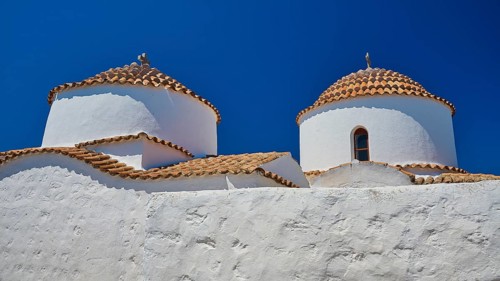 Two white painted church towers with red tiled roofs and small windows, bright blue sky, Chora, Old