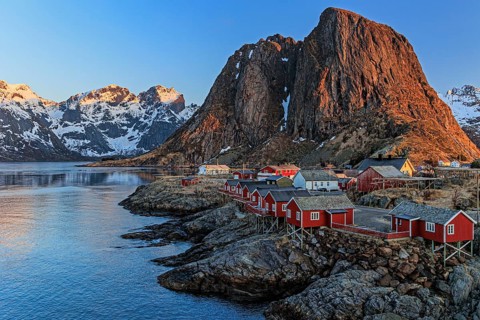 Typical Norwegian houses in fjord in front of steep mountains, morning light, winter, Reine,