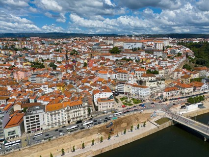 Wide angle shot of a city with tiled roofs and river, surrounded by hills and a sky with clouds,