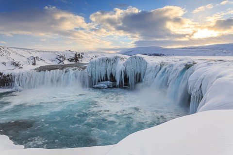Icy waterfall and rapids in front of a mountain landscape, cloudy mood, snow, Godafoss, Isla