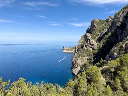 Rugged cliffs overlooking the deep blue sea, crossed by a boat on the water, Cala d'en Sardina,