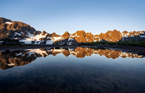 Rocky mountain peaks reflected in a small pond, mountain landscape with alpenglow at sunrise, at