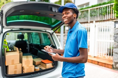 African delivery man in blue uniform verifying the packages on a van standing in the street