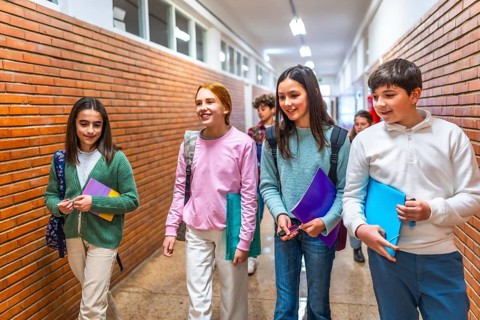 Cheerful students carrying books and folders are walking down school hallway between classes,