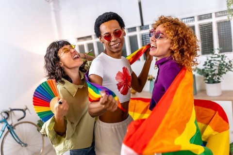 Lesbian couple and transgender friend laughing, singing and dancing, celebrating pride at home