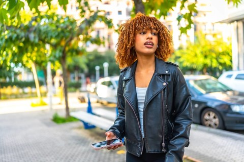 Distracted beauty latin woman listening to music with earbuds and smartphone outdoors in the street