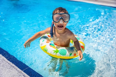 Happy playful caucasian boy with snorkel goggles and rubber ring on the swimming pool