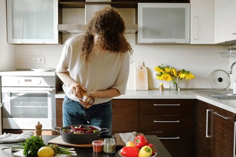 Woman sprinkles salt from manual spice mill on vegetables in a baking pan