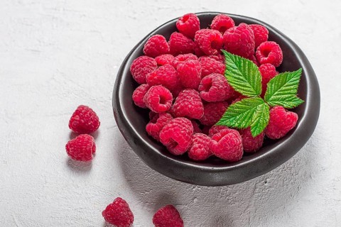 Fresh raspberries, on a black plate, with leaves, top view, on a white table