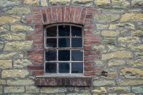 Single window embedded in a masonry stone wall with brick frame in an old farmhouse, North