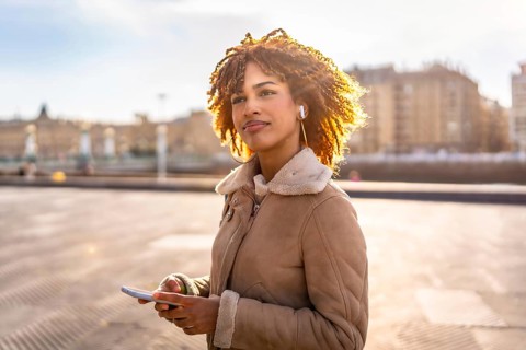 Latin beauty woman listening to music with earbuds and mobile phone outdoors in the city during