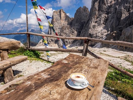 A cup of cappuccino, tibetian flag of prayer, mountain hut Rifugio Mulaz, Pala mountain group in