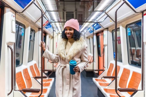 Smiling young black woman wearing winter coat and pink woolen hat holding reusable coffee cup