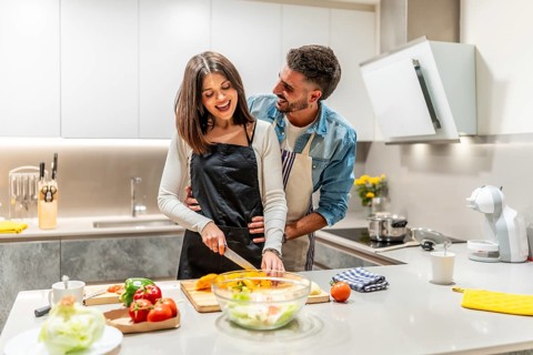 Young smiling couple wearing aprons preparing a healthy vegetable salad together in their modern