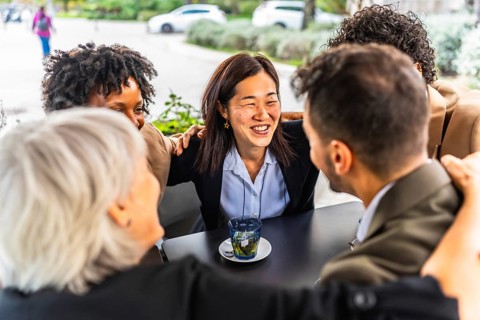 Successful team of multi-ethnic business people celebrating embracing form the shoulder sitting in