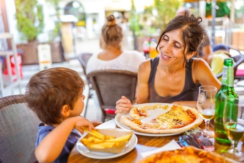 Mother and son sharing a meal of pizza and french fries at an outdoor restaurant, enjoying their