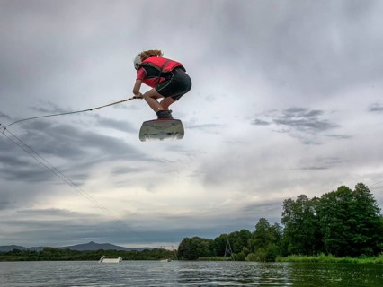 Boy or girl flies over the lake, jump with wakeboard, red life jacket, water skiing in wakepark,