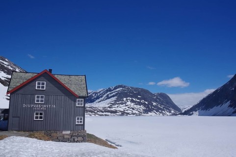 Mountain hut in a snow-covered late winter landscape, surrounded by mountains and a frozen lake,