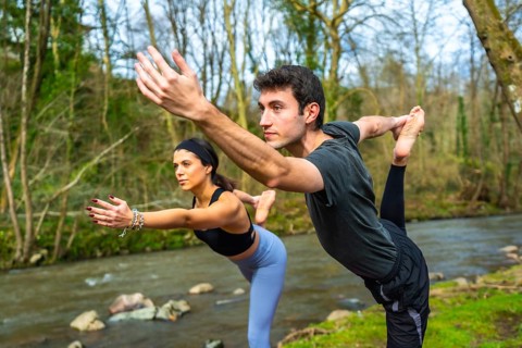 Yoga instructors performing a balancing pose by a river, showcasing flexibility and mindfulness in
