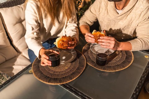 Couple sharing a relaxed moment, eating burgers and drinking beverages at a glass table, creating a