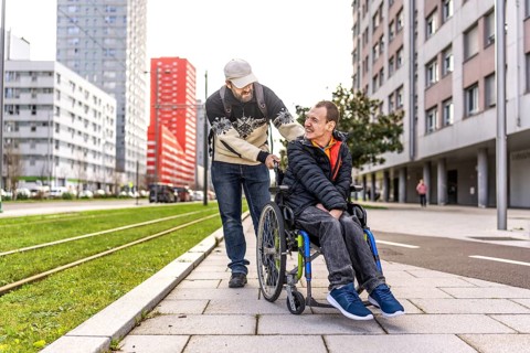 Caregiver assisting a young man with disability, strolling through a city environment, promoting