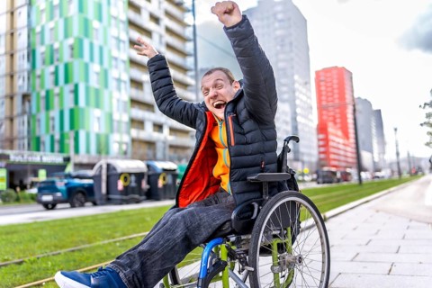 Young man in a wheelchair, raising his arms in celebration, embracing freedom and joy in a vibrant