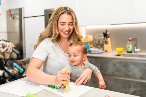 Happy mother and her baby son enjoying creative time, painting together in their bright modern