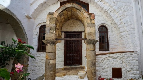Entrance of a building with ancient columns and a round arch, surrounded by flowers and stone