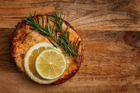 Salmon steak, fried, on a cutting board, top view, rosemary, lemon and lime, homemade, one serving,