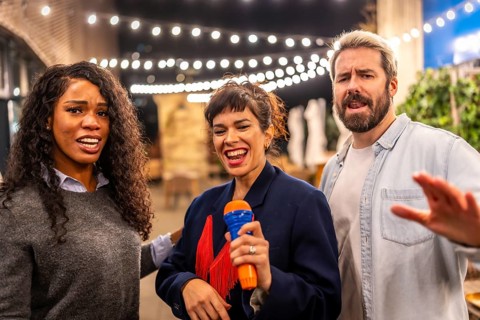 Multi-ethnic happy friends complain while woman singing karaoke at night party in a bar terrace