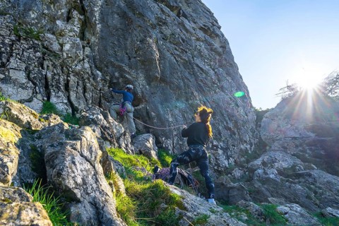 Two female rock climbers scaling a steep cliff face, illuminated by bright sunlight, showcasing