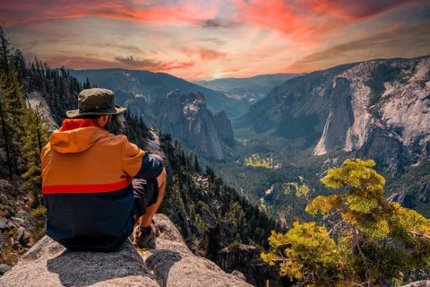 A young man on the trek sitting on the Sentinel Dome lookout in Yosemite National Park looking at