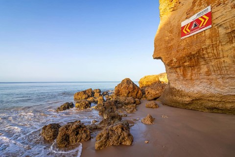 ROCKFALL UNSTABLE CLIFFS, KEEP A SAFE DISTANCE is written in English on a warning sign in Portugal