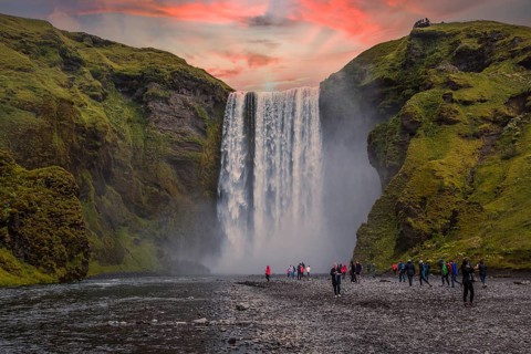 Group of tourists looking at the beautiful rainbow at the impressive Skogarfoss waterfall in