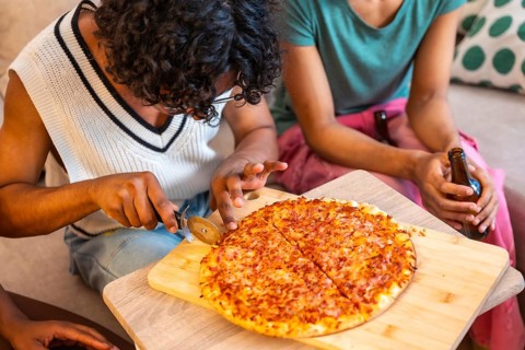Close-up of man cutting homemade pizza to share with friends at home