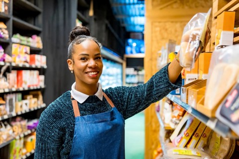 Friendly saleswoman arranging gluten free products on shelves, working in an organic supermarket,