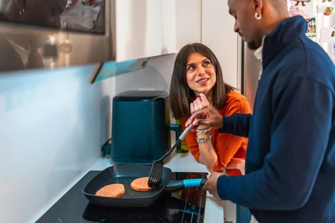 Happy multiethnic couple preparing burgers in a pan in their modern kitchen, enjoying their time