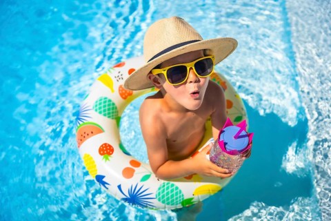 Top view of an expressive caucasian boy wearing sunglasses and sun hat playing inside a pool with