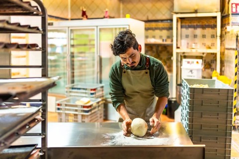 Latin young male baker kneading the raw dough in the kitchen of an artisan workshop