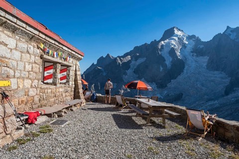 Moutain hut Cabane de l'A Neuve, tourists sitting on terrace, Aiguille Rouges du Dolent massif at