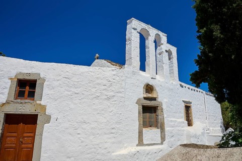 White church with bell tower and wooden door in front of a bright blue sky, Chora, Old Town,