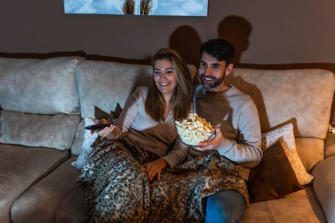 Young couple enjoying a movie night at home, sharing popcorn and relaxing on the sofa under a