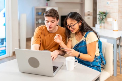 Multiethnic couple making online purchases using laptop and credit card, enjoying a convenient and