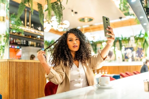 Latin sensual woman touching her curly hair while taking selfie at cafeteria