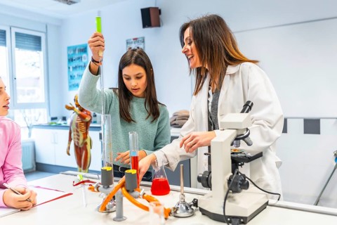 Female teacher assisting student using laboratory equipment during a chemistry experiment in a